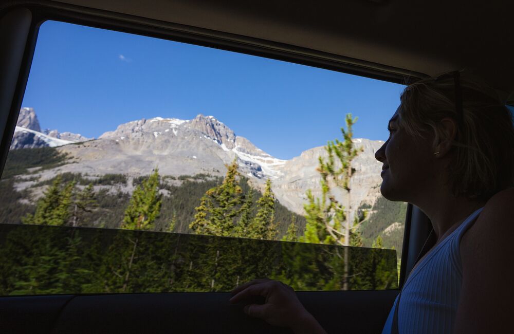 A women looks out the car window at the mountains on the Icefields Parkway in Banff National Park during a road trip.